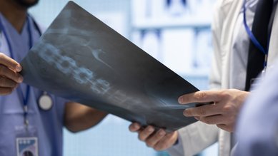 Zwei medizinische Fachkräfte betrachten gemeinsam ein Röntgenbild der Wirbelsäule in einem klinischen Umfeld.
