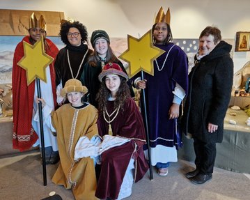 Sechs Personen in festlicher Kleidung stehen zusammen, einige halten große Sterne. Eine Frau steht rechts, während die anderen in der Mitte posieren.