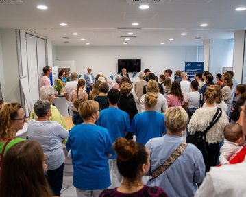 Eine große Gruppe von Menschen steht in einem Raum und hört einer Präsentation zu, während einige Personen auf der Bühne sprechen.