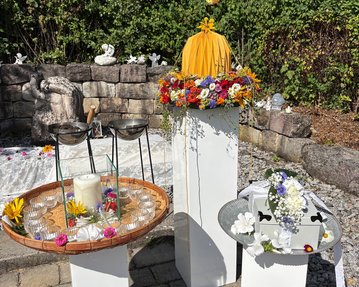 Ein dekorierter Bereich mit drei weißen Ständern, einem Tablett mit Kerze und Blumen sowie einem mit einer Blumenschmuckbox.