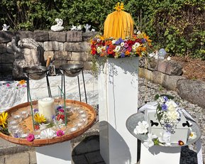 Ein dekorierter Bereich mit drei weißen Ständern, einem Tablett mit Kerze und Blumen sowie einem mit einer Blumenschmuckbox.