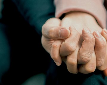 Zwei Hände halten sich fest, eine Hand umschließt die andere. Die Hauttöne sind unterschiedlich, und die Hände sind in einer engen Umarmung positioniert.