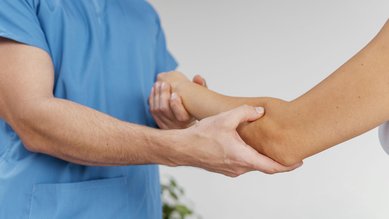 Ein Arzt in blauer Kleidung hält den Arm eines Patienten und führt eine Untersuchung oder Behandlung durch.