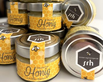 Mehrere Gläser mit deutschem Honig, etikettiert mit einem gelben Design und dem Schriftzug "Deutscher Honig von SRH-Bienen".