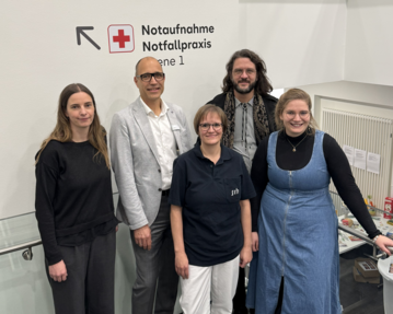 Fünf Personen stehen in einem modernen Innenraum vor einem Schild mit der Aufschrift „Notaufnahme Notfallpraxis“.