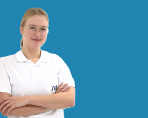 Eine lächelnde Frau mit Brille trägt ein weißes Polohemd und steht mit verschränkten Armen vor einem blauen Hintergrund.