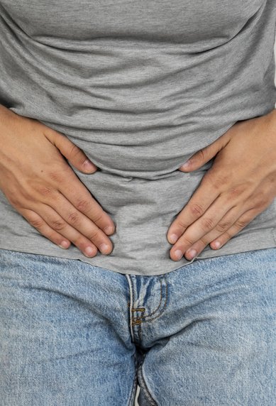 Mann mit grauem T-Shirt hält sich den Bauch, möglicherweise aufgrund von Unwohlsein oder Schmerzen.