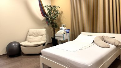 Ein Schlafzimmer mit einem weißen Bett, einem Sessel, einem Gymnastikball und einer Pflanze. Eine Hängematte ist an der Wand befestigt.