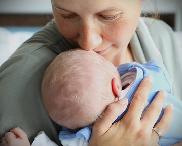 Eine Mutter küsst ihr neugeborenes Baby, das in ihren Armen liegt, während sie liebevoll auf es schaut.
