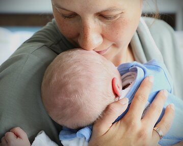 Eine Mutter küsst ihr neugeborenes Baby, das in ihren Armen liegt, während sie liebevoll auf es schaut.