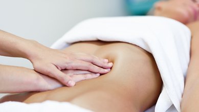 Eine Person erhält eine Bauchmassage, während sie auf einer Liege liegt, mit einem Handtuch bedeckt.