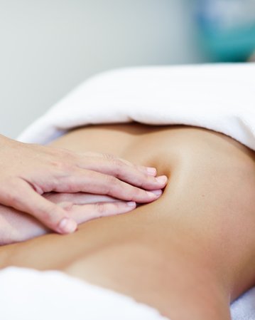 Eine Person erhält eine Bauchmassage, während sie auf einer Liege liegt, mit einem Handtuch bedeckt.