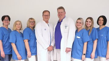 Eine Gruppe von zehn medizinischen Fachkräften in blauen Uniformen, darunter zwei Ärzte in weißen Kitteln, posiert für ein Gruppenfoto.