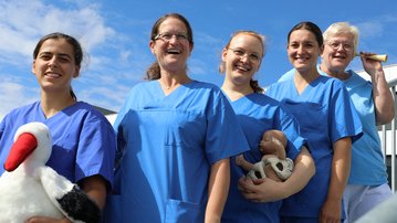 Fünf Personen in blauen Arbeitskleidung stehen lächelnd im Freien, einige halten Stofftiere in den Händen.
