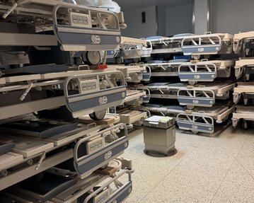 Ein Raum mit mehreren Krankenhausbetten, ordentlich gestapelt und bereit zur Nutzung. Ein kleiner Tisch steht in der Mitte.