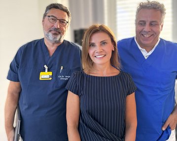 Drei medizinische Fachkräfte stehen zusammen, zwei Männer in blauen und schwarzen Kitteln und eine Frau in gestreiftem Oberteil, lächelnd.