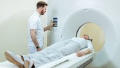 Ein Arzt bedient ein CT-Gerät, während ein Patient auf der Liege liegt und sich auf die Untersuchung vorbereitet.