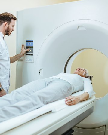 Ein Arzt bedient ein CT-Gerät, während ein Patient auf der Liege liegt und sich auf die Untersuchung vorbereitet.